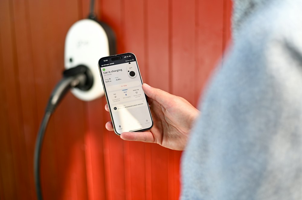 Hand steuert mit dem Smartphone das Laden über eine Wallbox