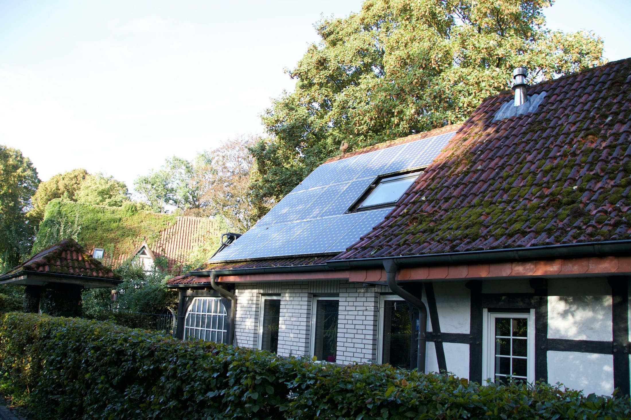 Fachwerkhaus mit Solarmodulen auf dem Dach hinter einer Hecke