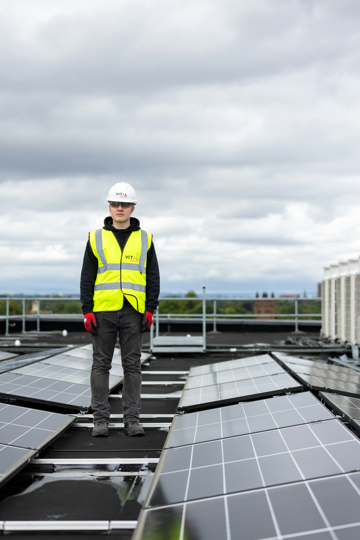 Techniker in Warnweste steht auf einem Dach mit Solarmodulen