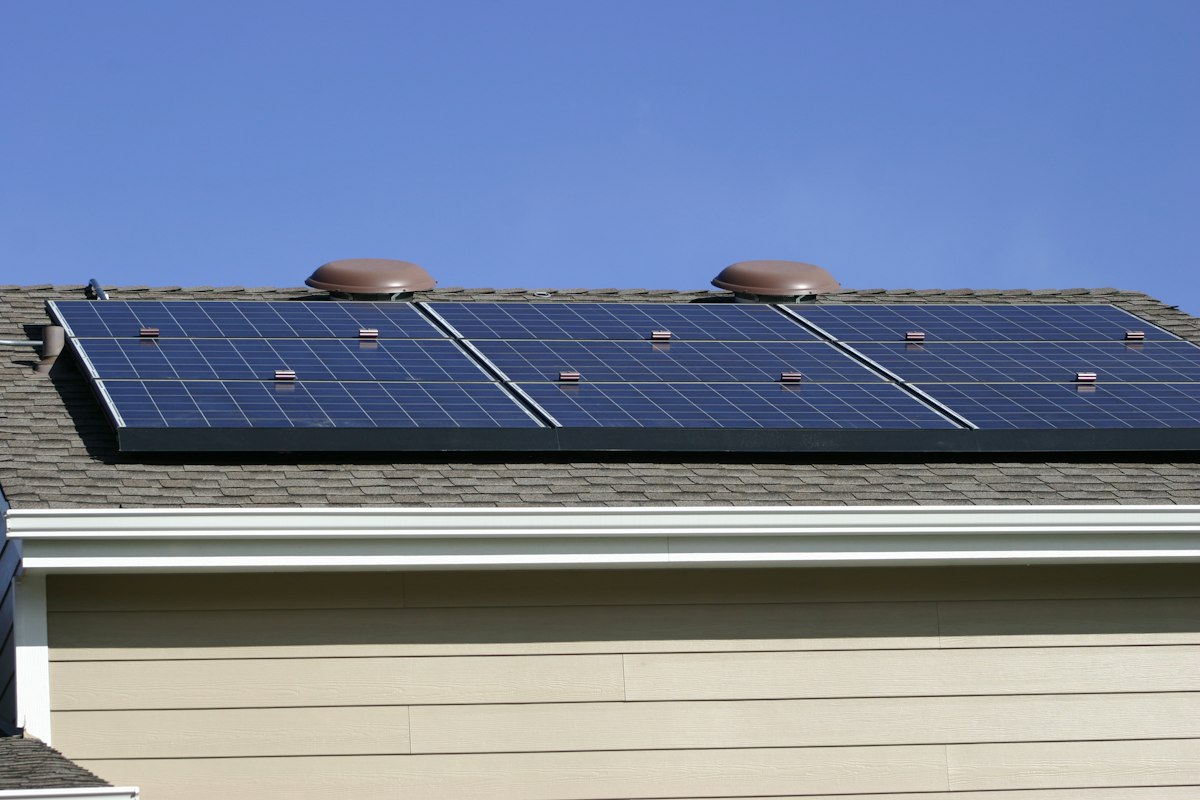 Hausdach mit einer Reihe Solarmodule vor blauem Himmel